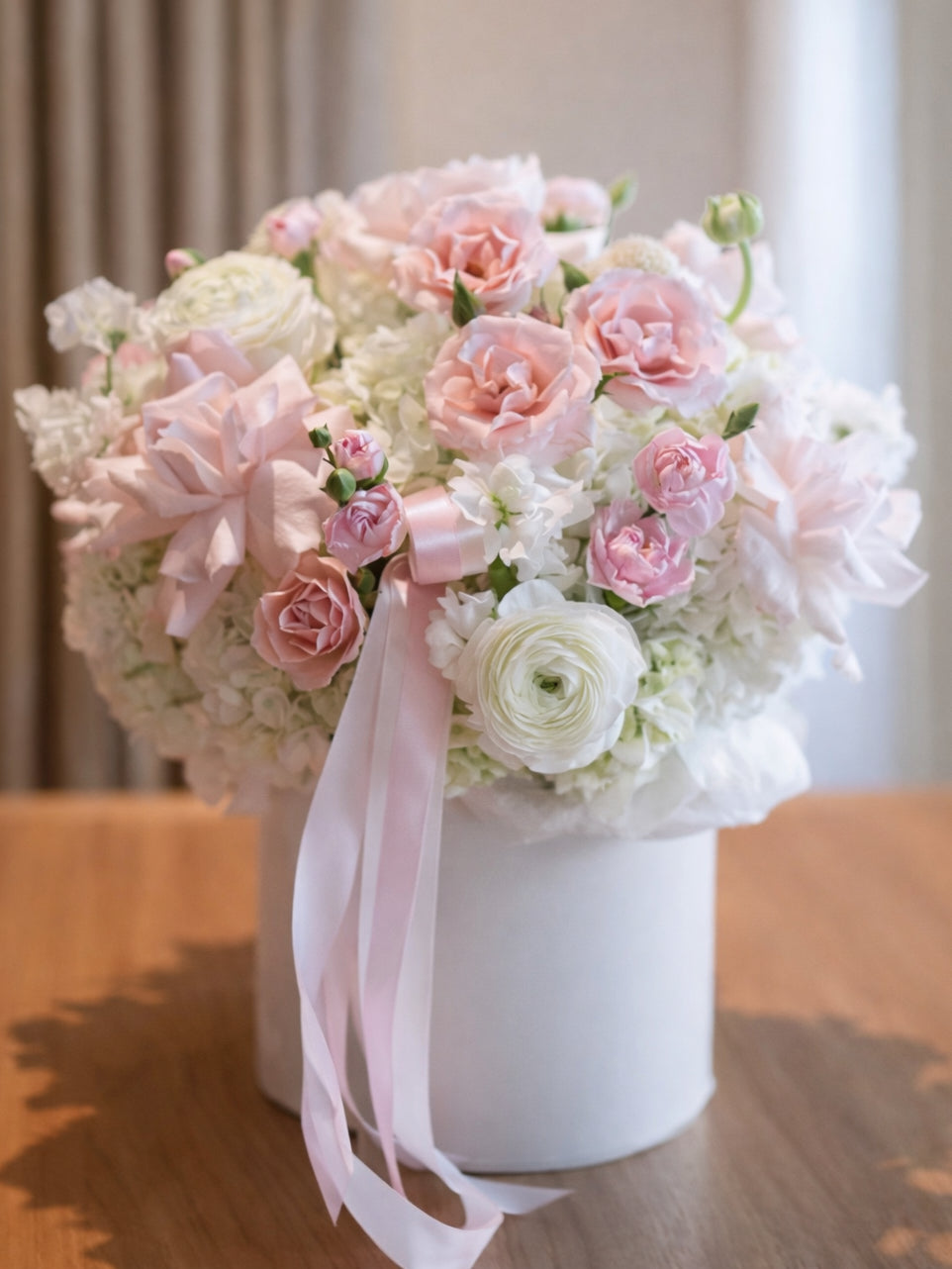 Bouquet of pink and white flowers in a white flower box with a pink ribbon on a wooden surface.