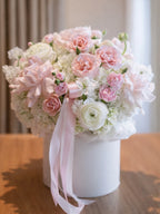 Bouquet of pink and white flowers in a white flower box with a pink ribbon on a wooden surface.
