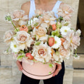 Luxury flower box with blush roses, peach ranunculus and white daisies, held by a florist
