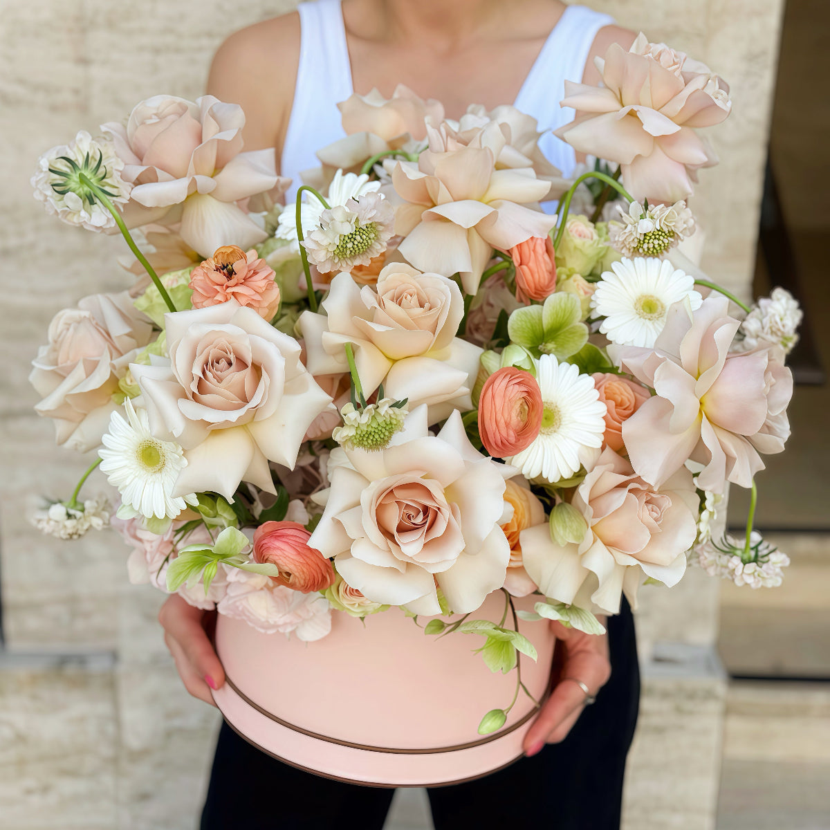 Luxury flower box with blush roses, peach ranunculus and white daisies, held by a florist
