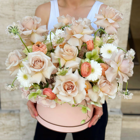 Luxury flower box with blush roses, peach ranunculus and white daisies, held by a florist