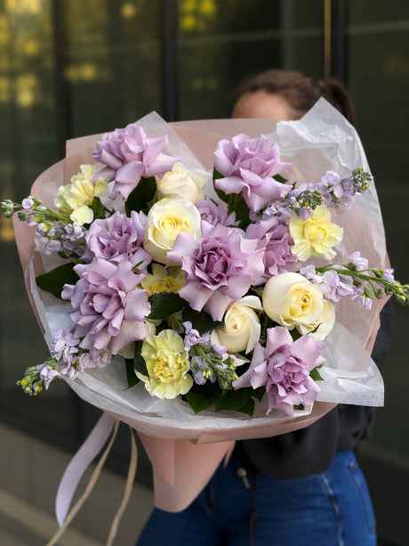 Bouquet of purple and yellow flowers held by a person with a blurred background