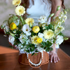 Bouquet of yellow and white flowers in a wicker basket held by a person.